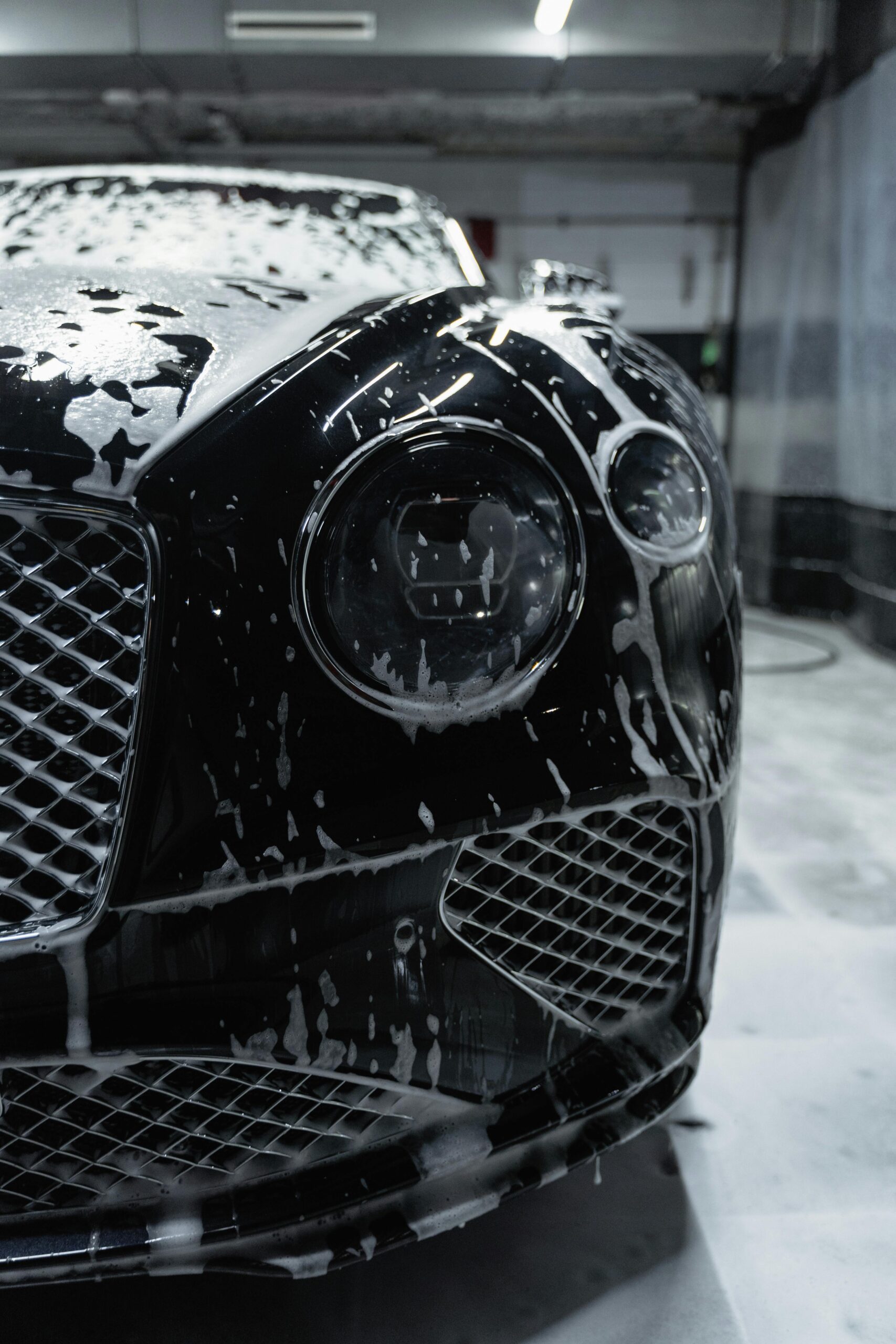 pexels photo 6872582 6872582 Close-up of a sleek black luxury car with soapy foam during a carwash process.